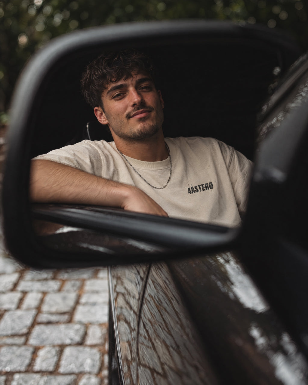 Young man in a natural 4ASTERO tee with the small chest logo, reflected in a car's side mirror